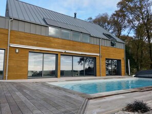 A modern house with a swimming pool, large sliding glass doors, and a wooden deck. - Villa Moderne Avec Piscine (Berric)