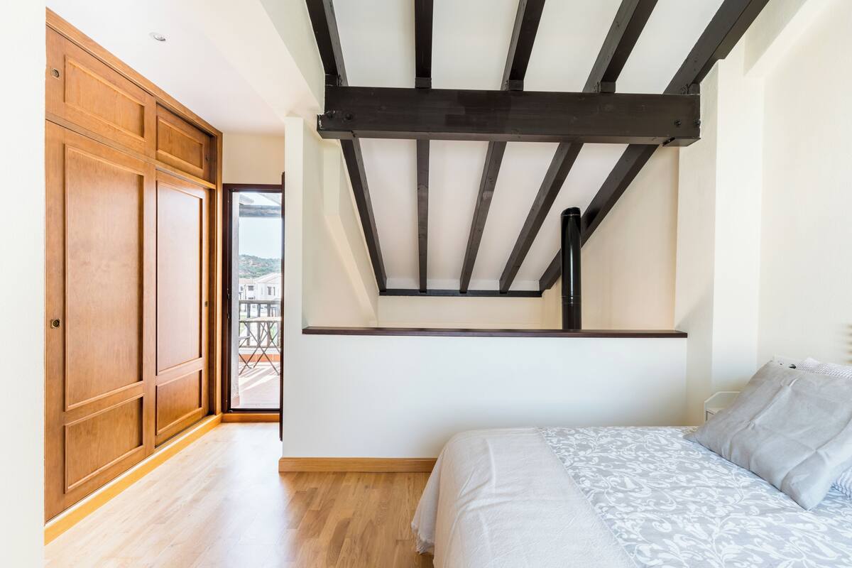 Ein Schlafzimmer mit einem Bett, einem Holzschrank und Blick durch eine Glastür.