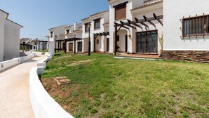 A row of white buildings with stone accents, a paved walkway, and a grassy area.