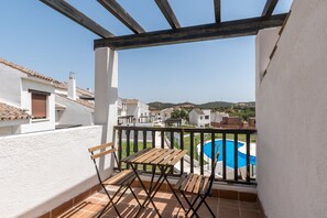 A balcony with a wooden table and chairs, overlooking a swimming pool and surrounding buildings.