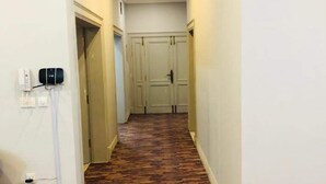 A hallway with a wooden floor, white walls, and a closed door at the end. - Rio Inn West (Mekhtar)
