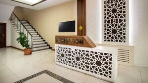 A reception area with a staircase, a flat-screen TV, and decorative panels. - Turkler Hotel (Trabzon)