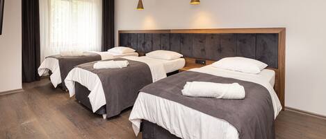 A hotel room with three beds, a wooden floor, and a modern design.