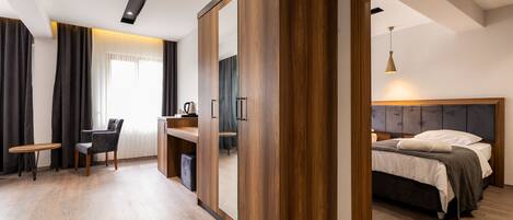A modern hotel room with a wooden floor, a desk with a chair, a bed with a headboard, and a large mirror.