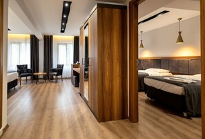 Una habitación de hotel moderna con piso de madera, un escritorio con sillas, una cama con cabecera y un espejo grande.