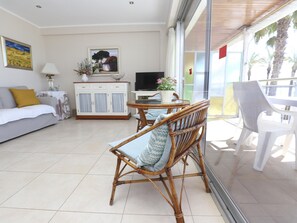 Una sala de estar moderna con un sofá, una mesa de comedor con sillas, un televisor y un balcón con vistas.