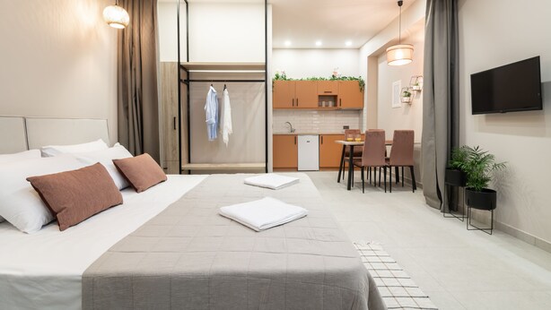 A hotel room with a bed, a desk, a chair, a TV, and a kitchenette.
