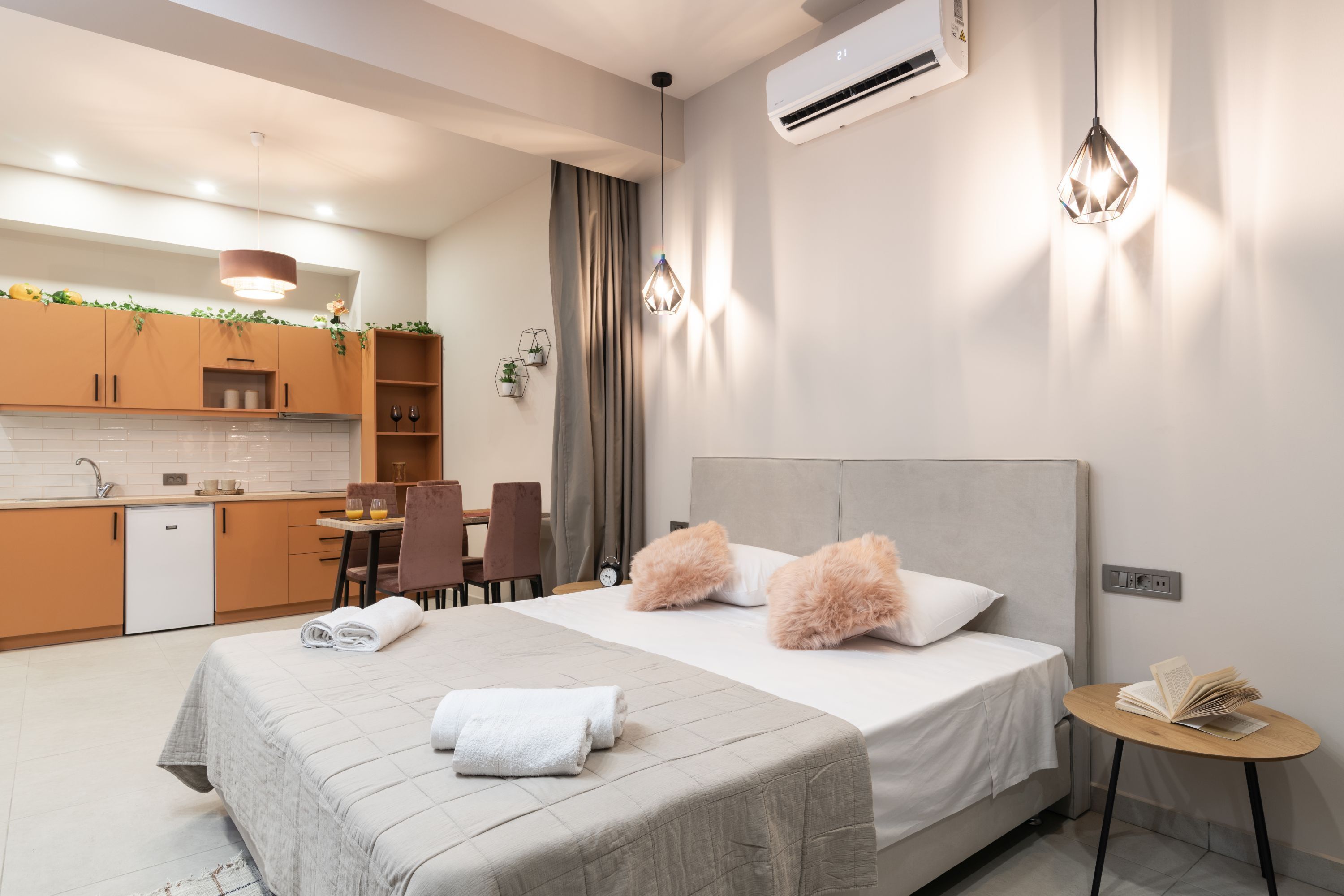 Ein modernes Hotelzimmer mit Bett, Nachttisch und einer kleinen Küchenzeile.