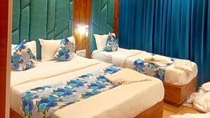 Habitación de hotel con dos camas, cabeceros tapizados en color turquesa, detalles de madera y un ventanal con cortinas azules.