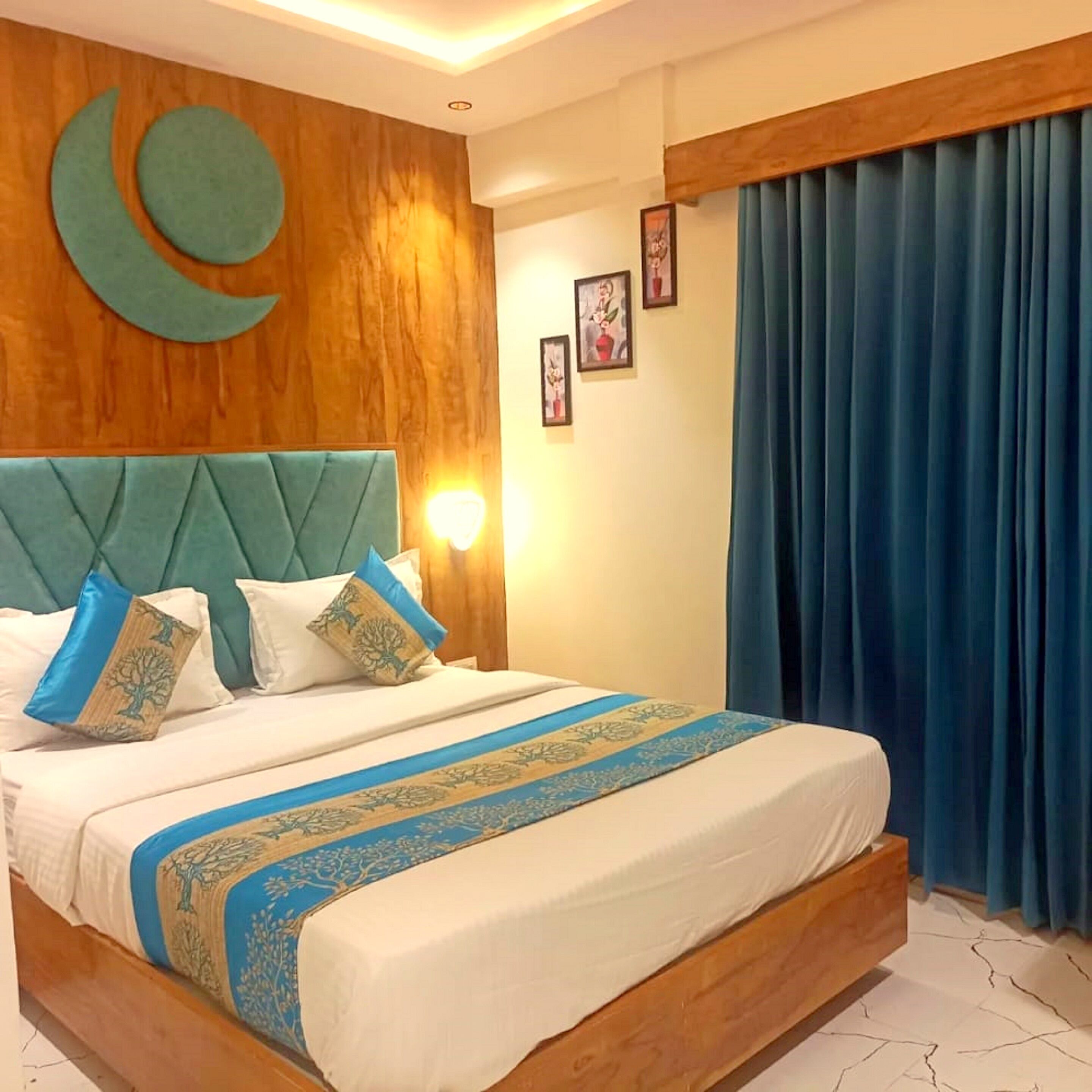 Habitación de hotel con cabecera de madera, cama con ropa de cama azul y blanca, cortina azul y cuadros en la pared.