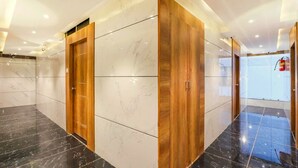 Un ascensor moderno con paredes de mármol y puertas de madera, que da a un pasillo bien iluminado con un extintor en la pared.