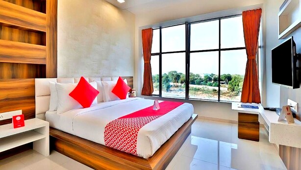 Una habitación de hotel moderna con una cama grande, televisión y ventana con cortinas.