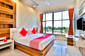 A modern hotel room with a large bed, a TV, and a window with curtains.