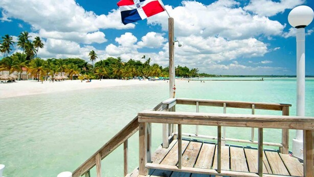 A wooden deck with a flag, a beach, and palm trees in the background. - Casa Durazno - Beautiful 3 Bed in Santo Domingo (Los Alcarrizos)