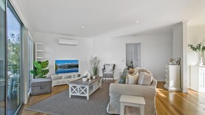 A modern living room with a flat-screen TV, a wicker chair, a sofa, and a coffee table.
