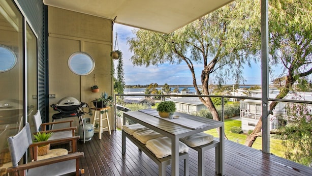 A balcony with a table, chairs, a grill, and potted plants.