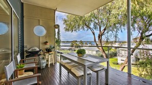 A balcony with a table, chairs, a grill, and potted plants.