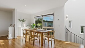 A dining area with a wooden table and chairs, a white cabinet, and a view of the outside through large windows.
