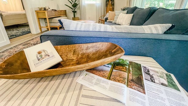A cozy living room with a blue sofa, a wooden bowl, and a magazine on a striped rug.