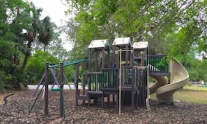 Explore a multi-level playground with climbing and sliding elements surrounded by trees.