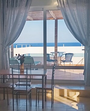 A room with a view of the sea, featuring a table and chairs, a vase with flowers, and a window with curtains. - Exquisite Retreat For Two (Rhodes)