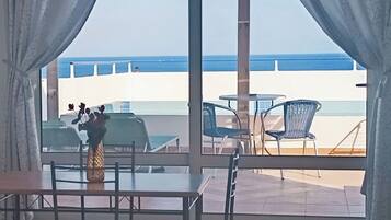 A room with a view of the sea, a dining table, chairs, and a vase with flowers.