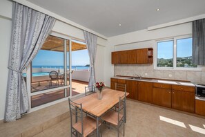 Uma cozinha moderna com armários de madeira, uma mesa de jantar com cadeiras e vista para o mar através de grandes janelas.
