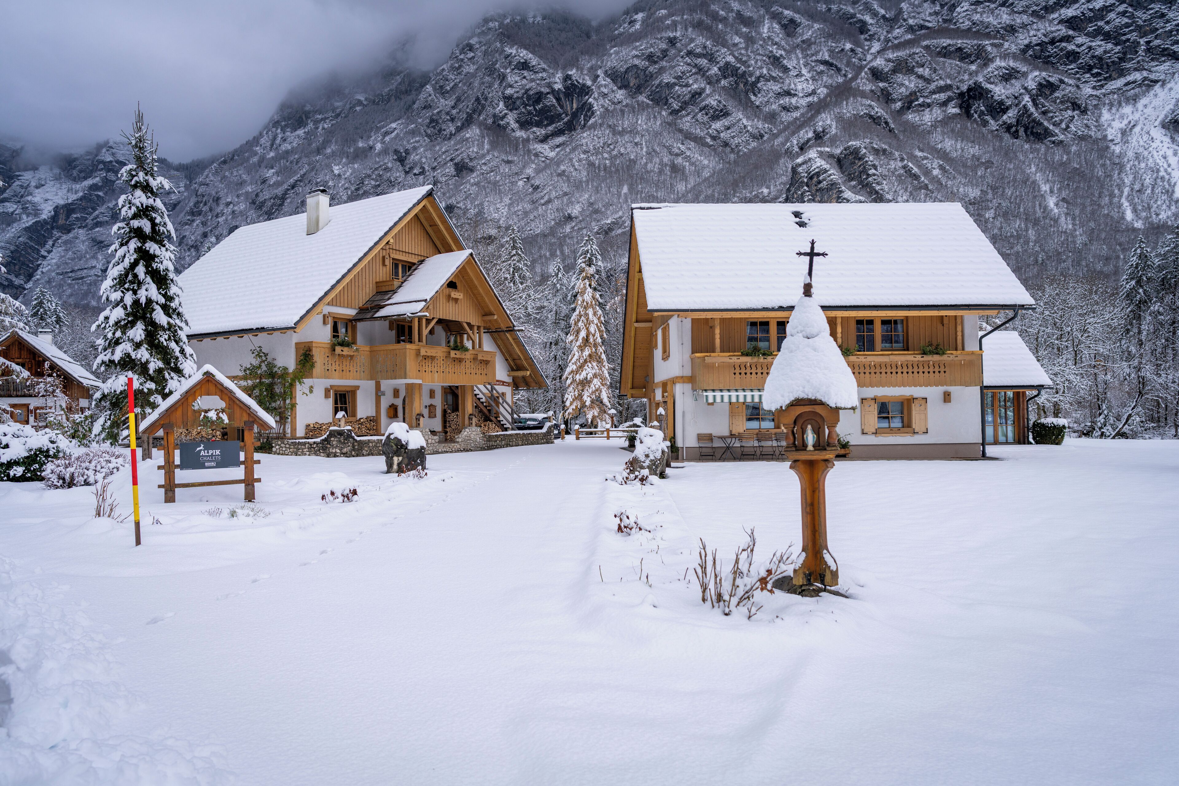 Un pueblo cubierto de nieve con casas de madera, un cartel que dice "Alpstein" y montañas al fondo.