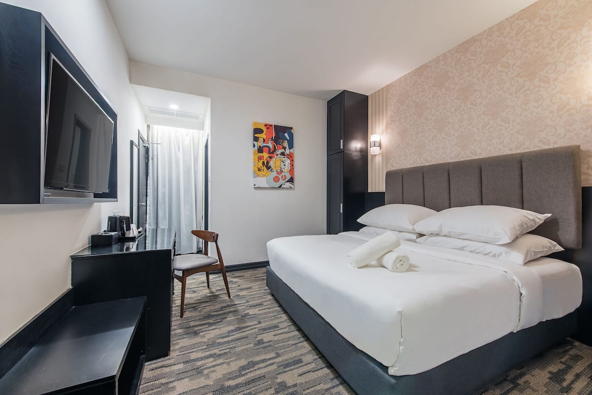 A hotel room with a bed, a desk, a chair, a television, and a painting on the wall.