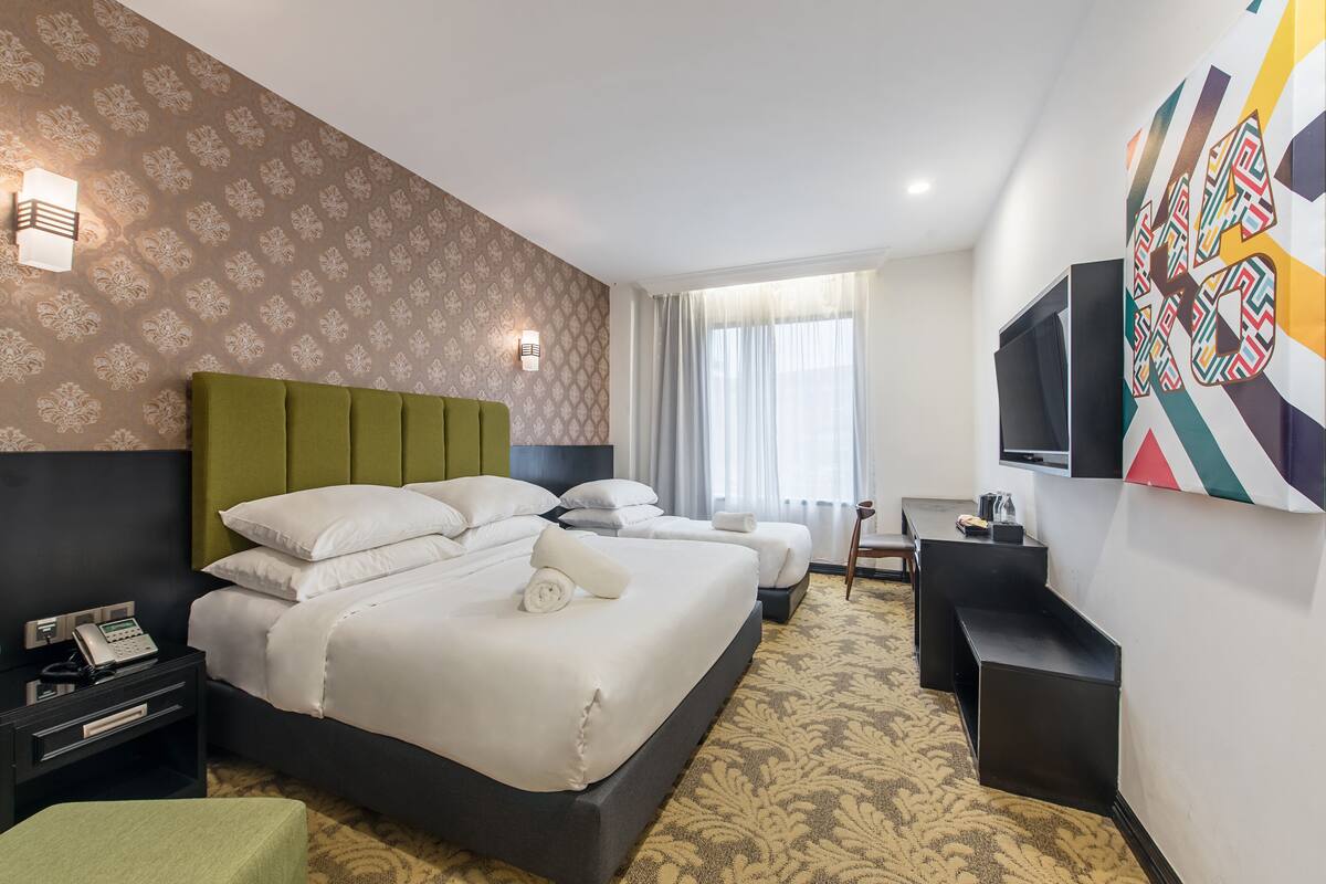 A hotel room with a large bed, two smaller beds, a desk, and a TV.