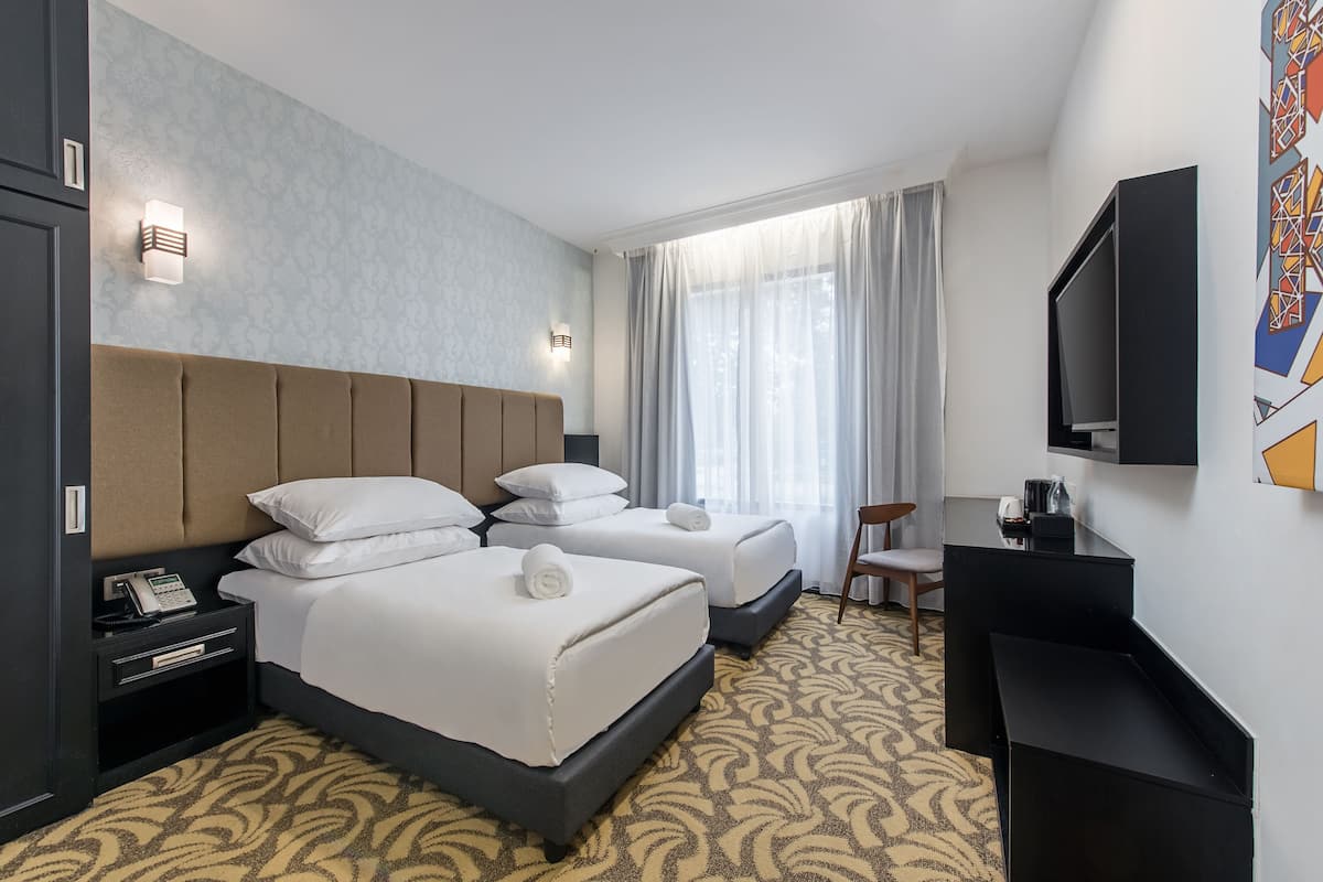 A hotel room with two beds, a desk, a chair, a TV, and a window with curtains.
