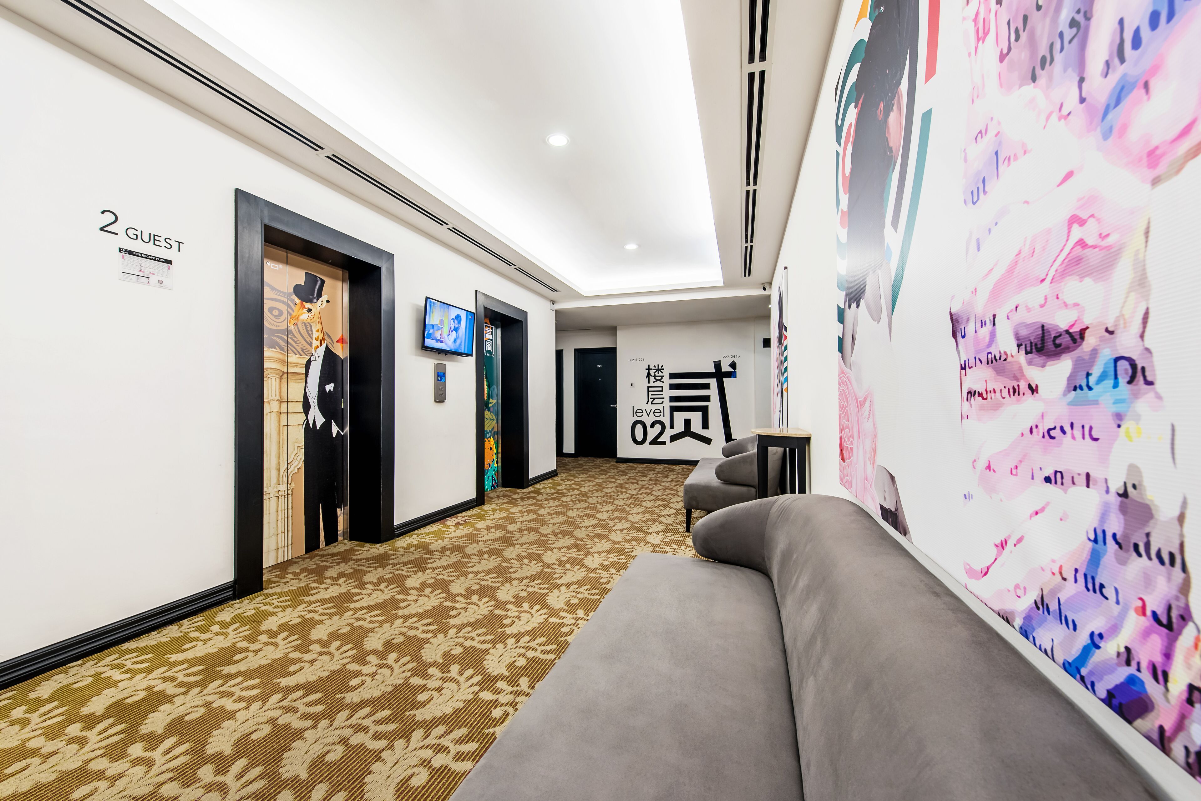 A modern hotel hallway with a patterned carpet, a sofa, and a wall with a colorful abstract design.