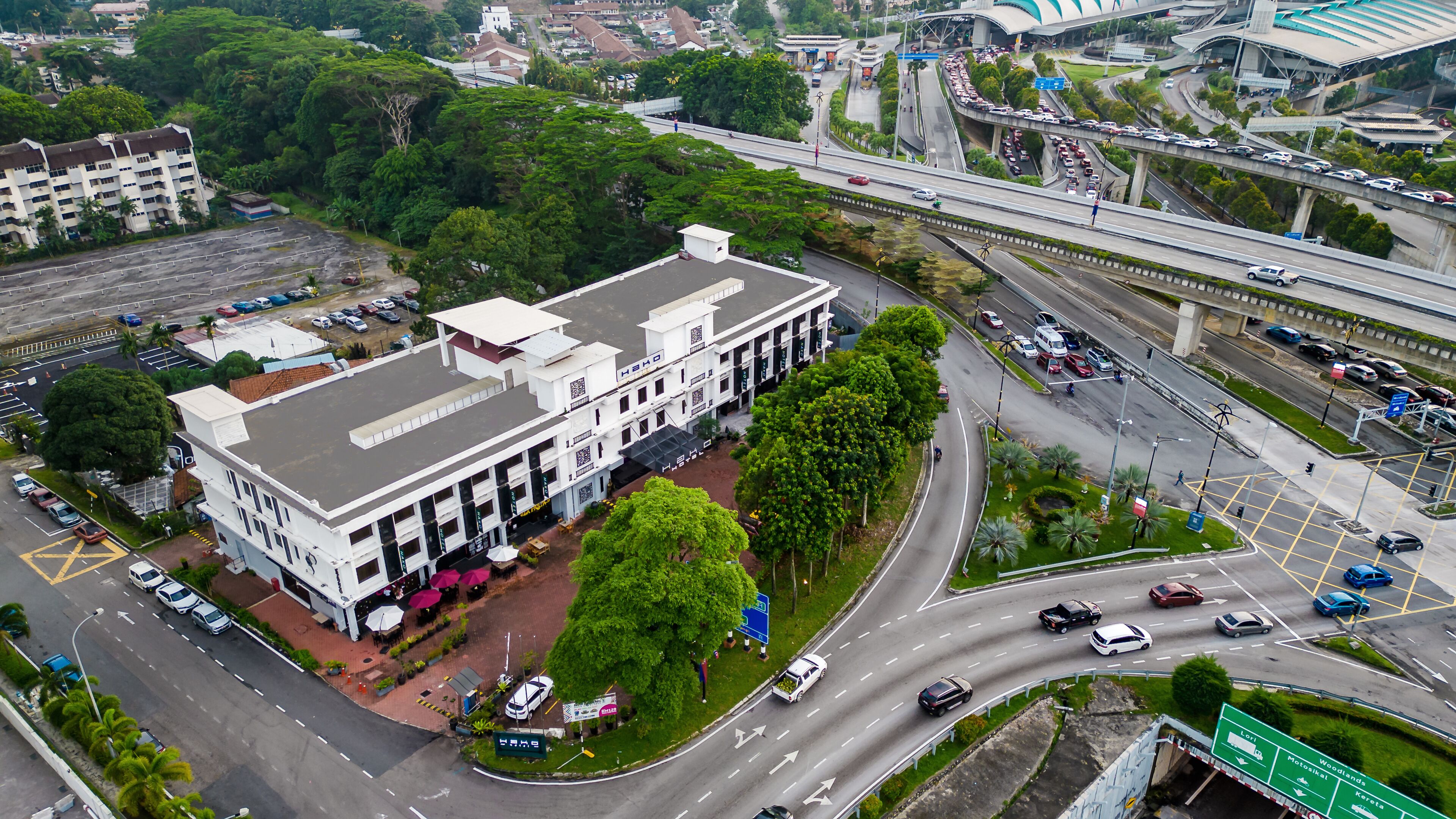 A large white building with multiple floors, surrounded by greenery and a parking lot.