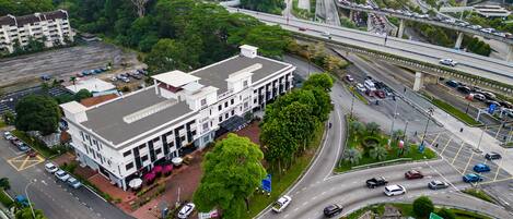 A large white building with multiple floors, surrounded by greenery and a parking lot.