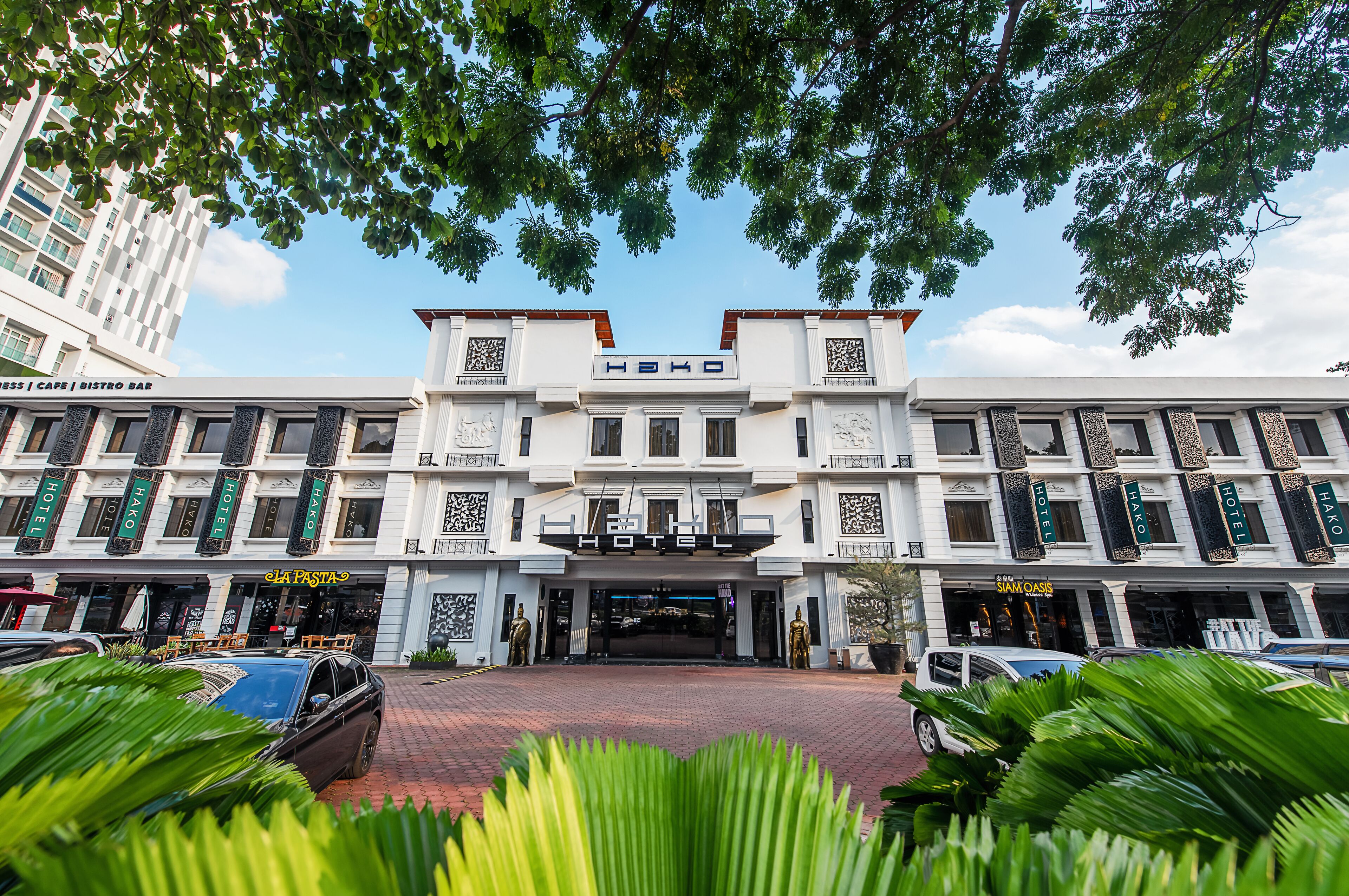 A hotel with a central entrance, multiple balconies, and a variety of shops on the ground floor.