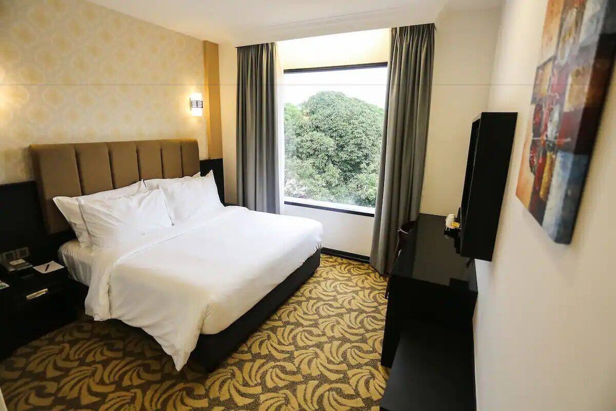 A hotel room with a bed, a nightstand, a desk with a chair, a TV, and a window with curtains.