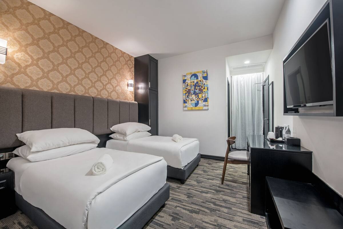 A hotel room with two beds, a flat-screen TV, a desk, and a patterned wall.