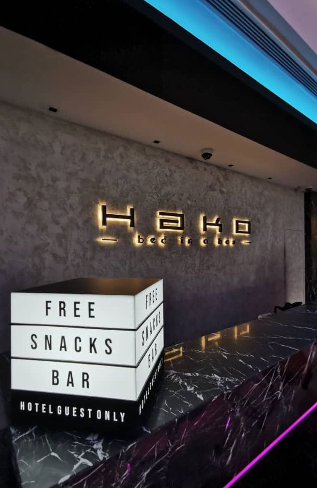 A hotel reception area with a sign reading "Hake Bed in a Bar" and a sign indicating "FREE SNACKS BAR HOTEL GUEST ONLY".