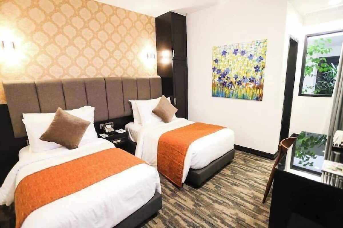 A hotel room with two beds, a headboard, a painting, a desk, and a chair.