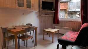 Un espacio habitable pequeño con una mesa de comedor, sillas, un sofá pequeño, un televisor montado en la pared y una ventana con cortinas.