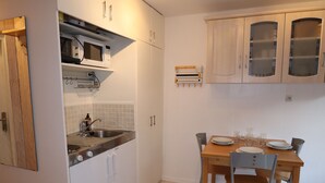 Cocina compacta con armarios blancos, un microondas y un lavamanos. Hay una mesa de comedor con sillas y una alfombra pequeña.