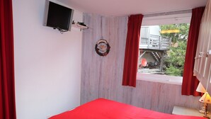 Un dormitorio con cama, televisor, ventana con cortinas y vistas a un balcón.