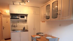 Cocina compacta con armarios blancos, un microondas y un lavamanos. Hay una mesa de comedor con sillas y una alfombra.