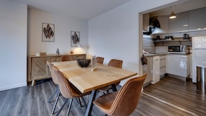 Een moderne keuken met een magnetron, fornuis en kastjes. Er is een eethoek met een houten tafel en stoelen.