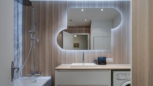 Een moderne badkamer met douche, wastafel, spiegel en een ingebouwde wasmachine.