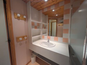 A bathroom with a white sink, a mirror, and a wooden ceiling.