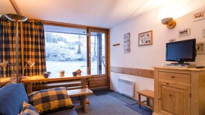Un accogliente interno di una baita con divano, panchetta in legno e televisore su un mobile.