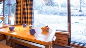 Un tavolo in legno con una panca, una finestra con tende a quadretti e vista su un'area esterna innevata.