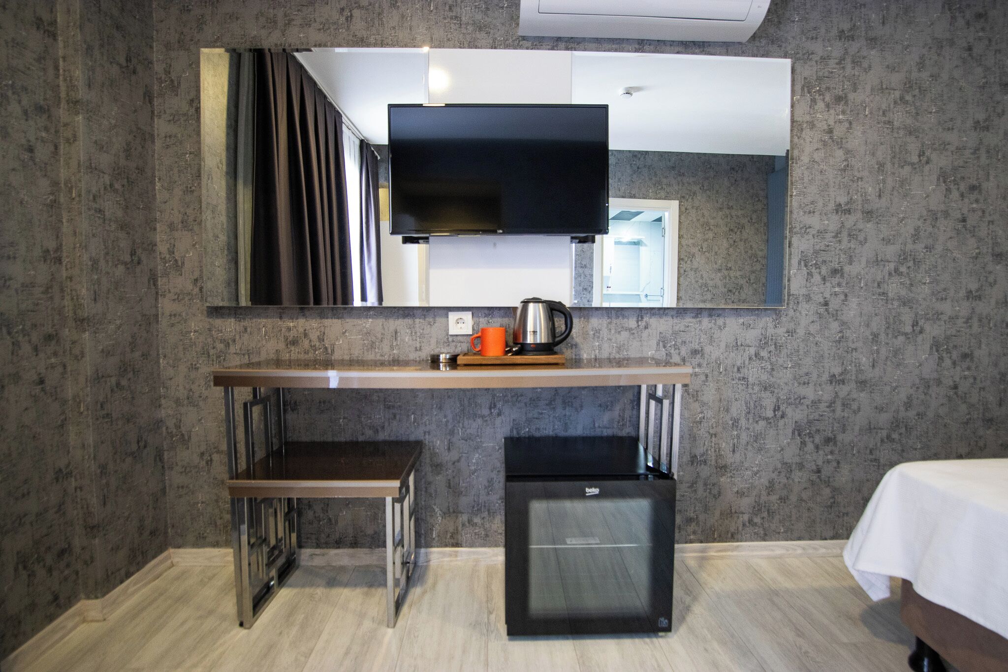 A compact hotel room with a kitchenette, a small refrigerator, a microwave, a coffee maker, and a bed with a white bedspread.