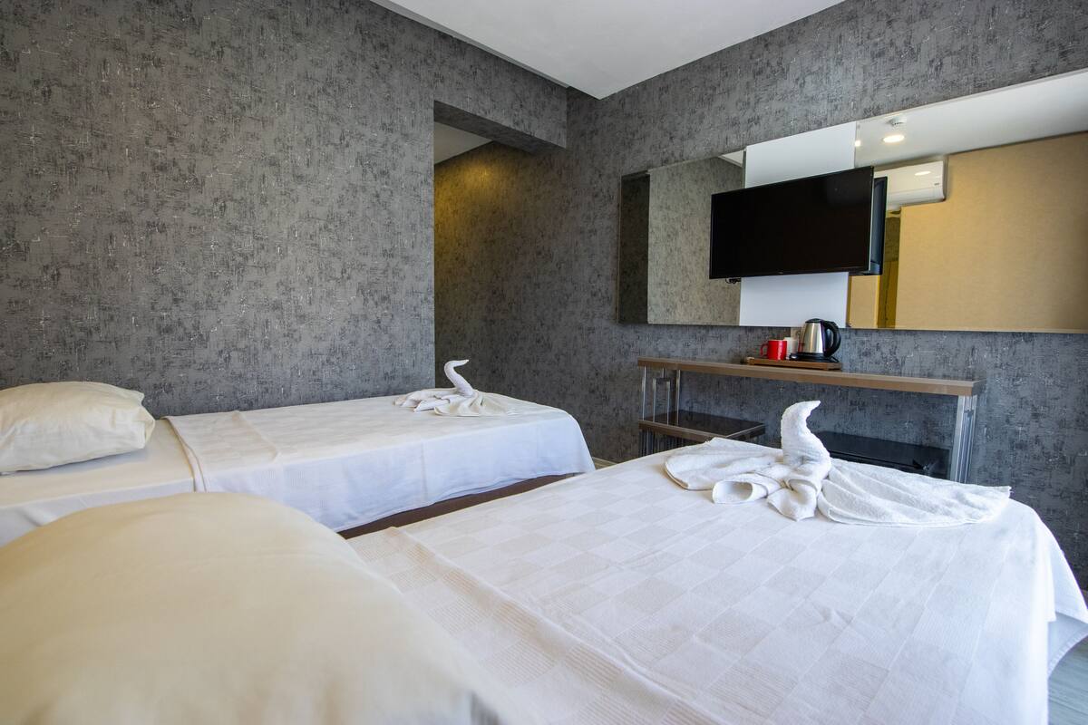 Ein Hotelzimmer mit zwei Betten, einem Wand-Fernseher und einem kleinen Tisch mit Wasserkocher und Tassen.